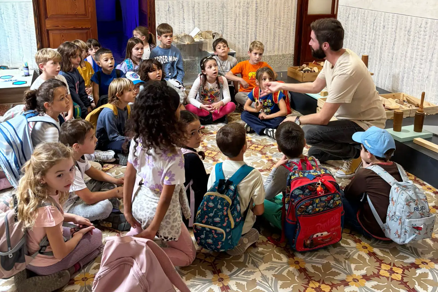 Un miembro del equipo de Can Prunera imparte un taller a un grupo de niños sentados en el suelo
